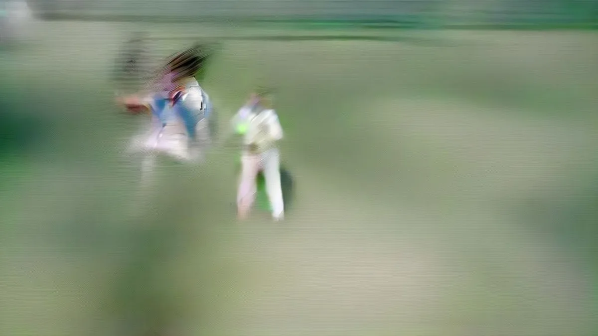 A professional cricketer executing a fluent cover drive during a red-ball match on a green pitch.