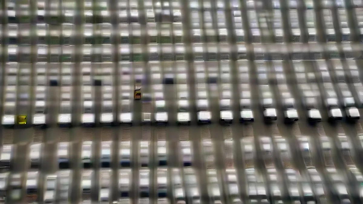 Rows of newly manufactured vehicles parked outside a production facility under overcast skies