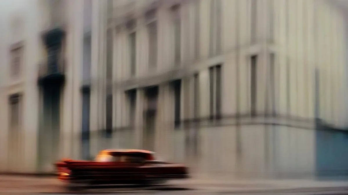 Vintage car driving down a residential street in Havana at dusk with weathered architectural facades in the background.