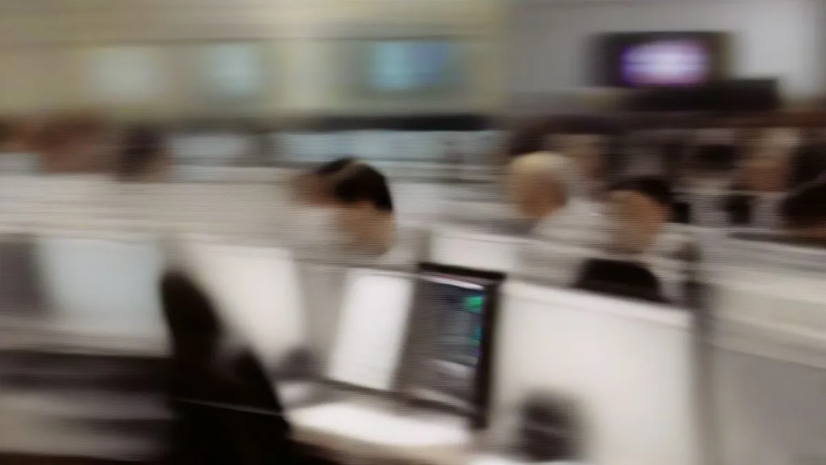 Financial market trader sitting at a multi-screen workstation on an active trading floor