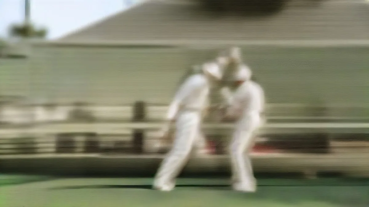 Two cricketers in white test uniforms conferring and tapping gloves on a cricket pitch under natural sunlight.
