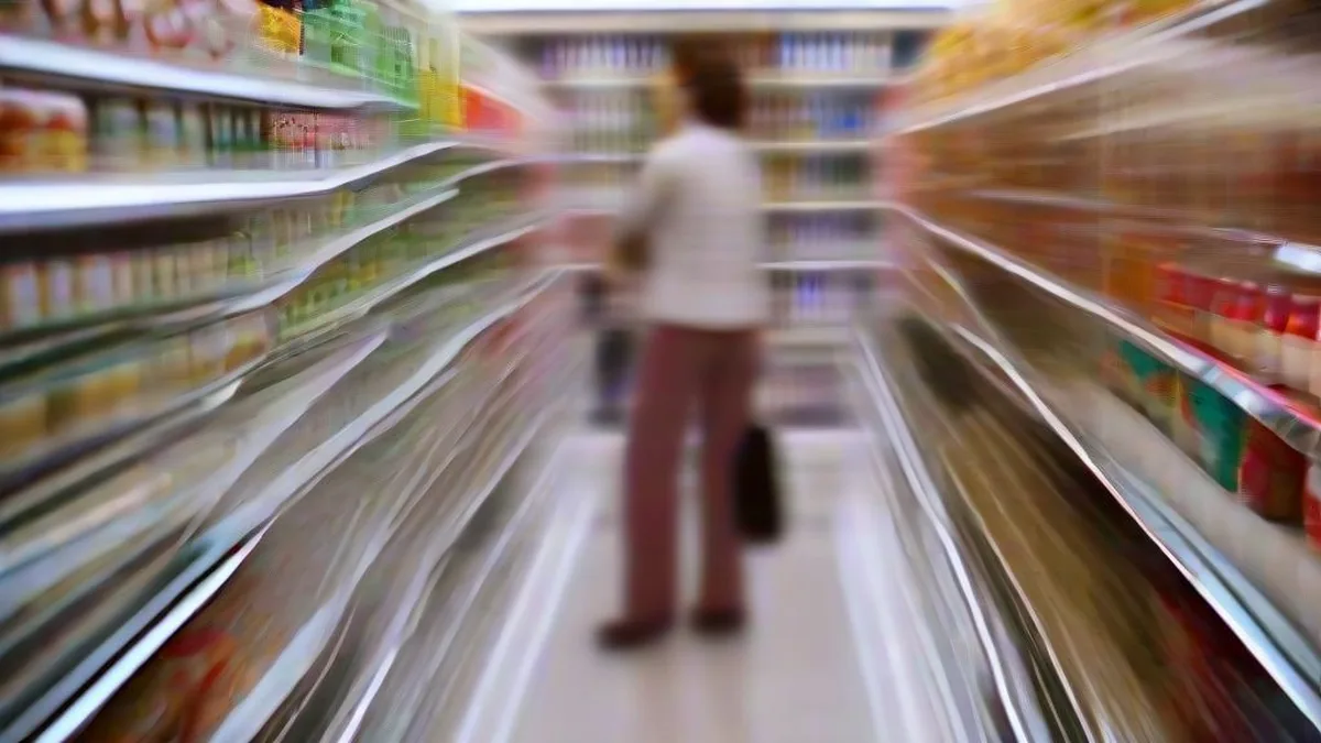 A shopper in a modern grocery aisle examining products on refrigerated shelves.