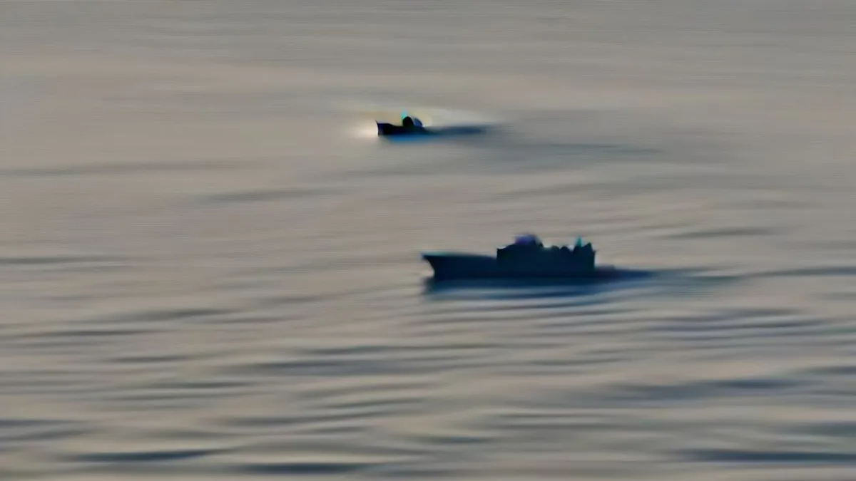 A large commercial oil tanker moving across open ocean waters with a distant naval patrol vessel on the horizon.