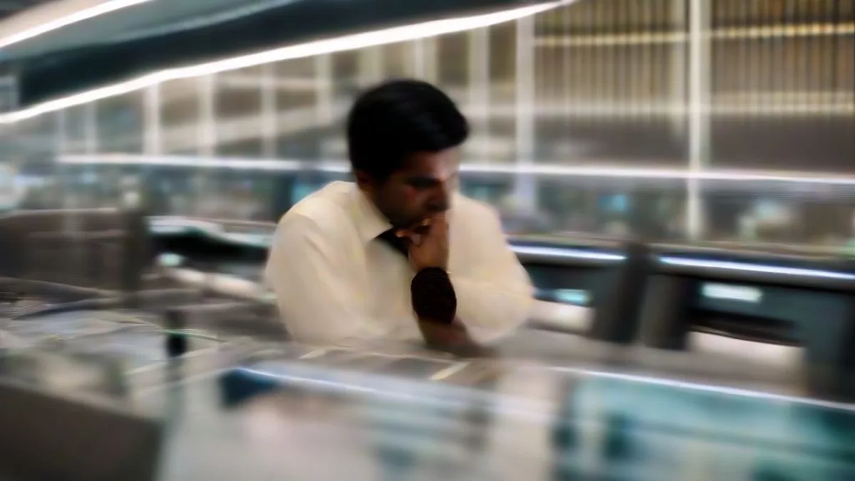 A financial trader at a desk observing computer monitors on a busy trading floor
