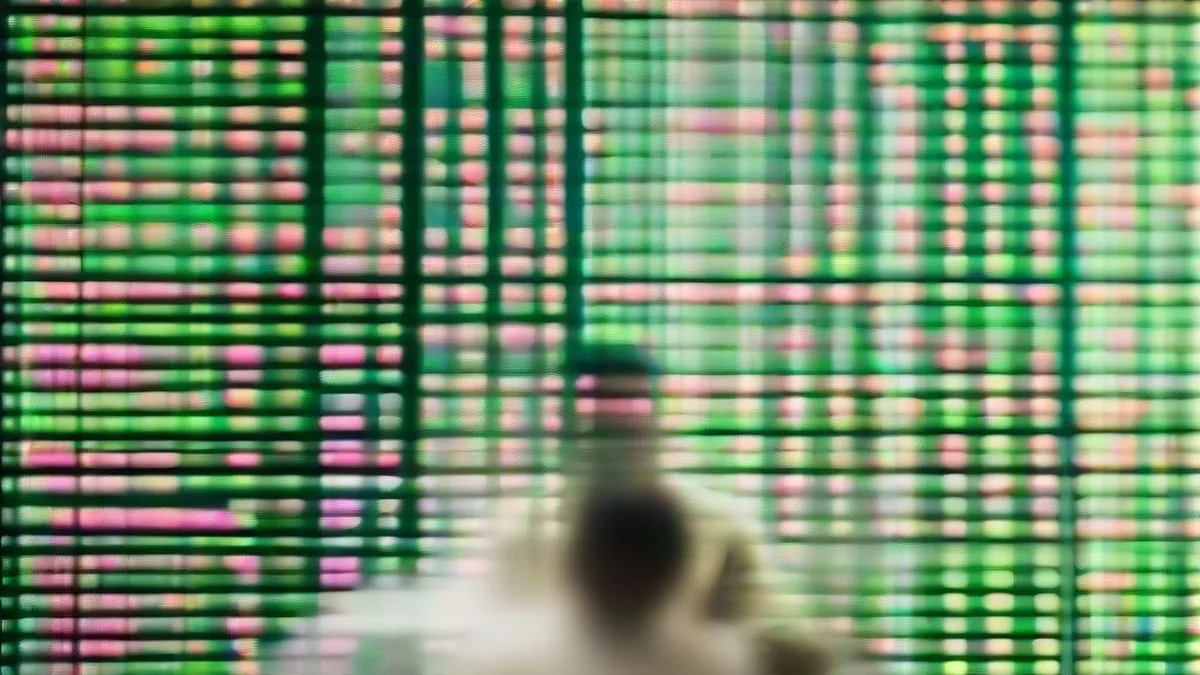 Financial trader sitting at a multi-monitor trading desk reviewing market indices in a modern office