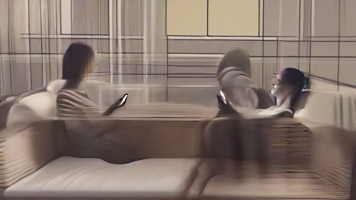 A person sitting on a sofa holding a smartphone next to wireless earbuds on a table